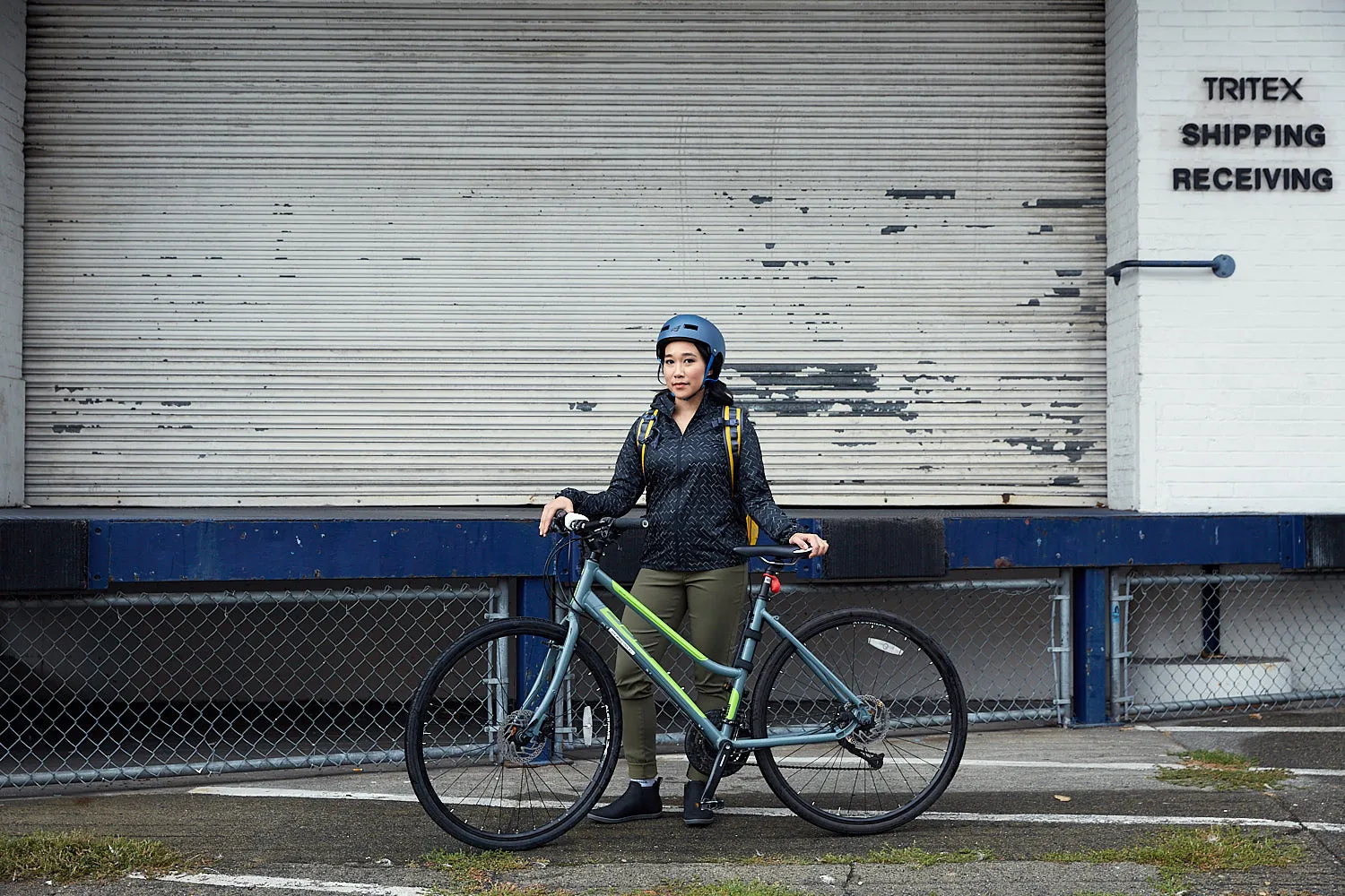 A woman stands with her bike in front of an industrial garage door.
