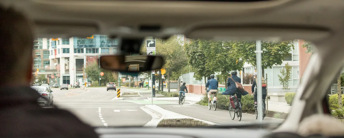 A person looks in their rearview mirror as they drive their vehicle. The road in front of them is seen through the windshield.