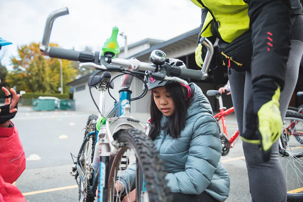A girl performs bike maintenance on her bike on school grounds.