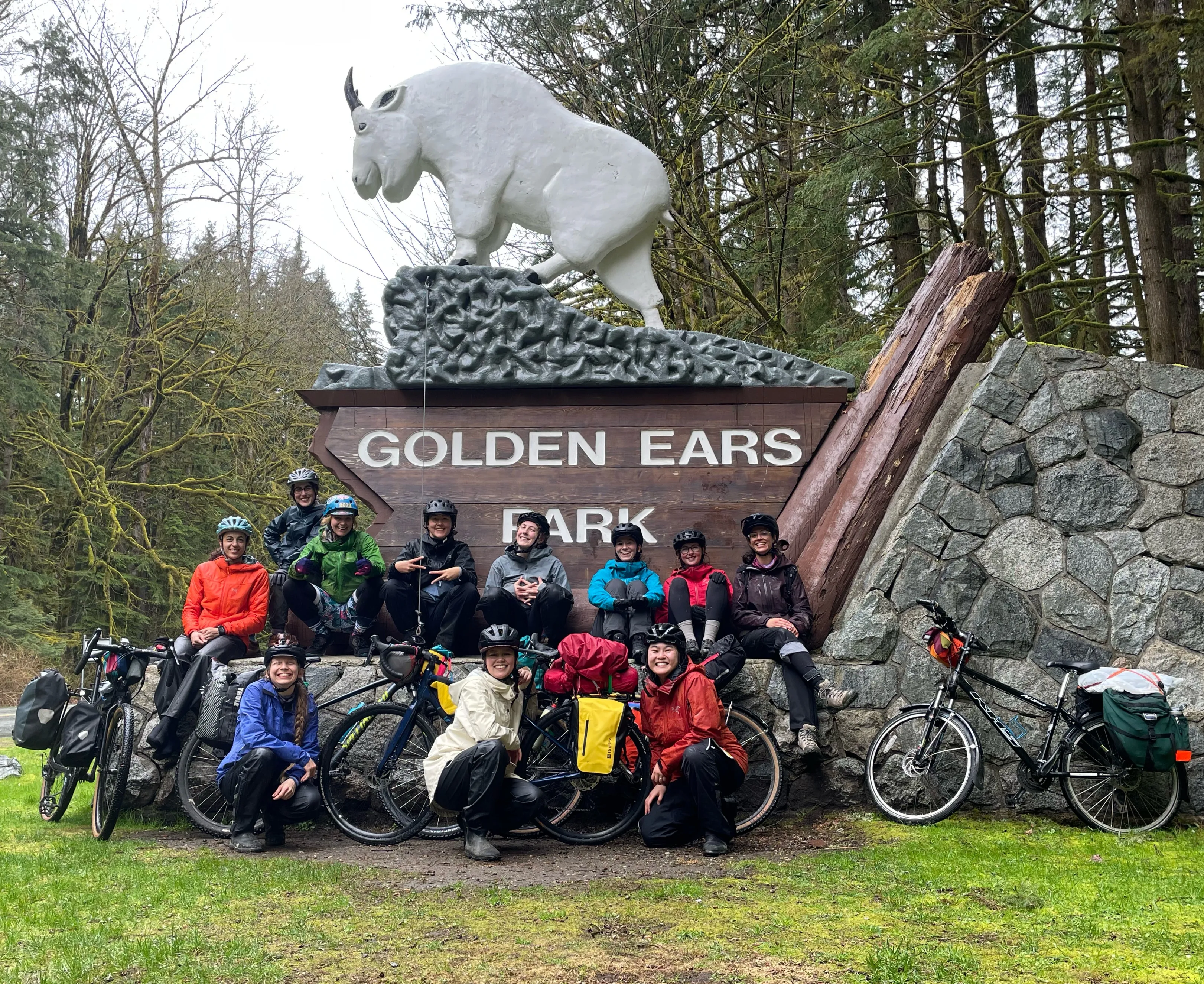 A group of women pose with their bikes in front of the 'Golden Ears Park' sign.