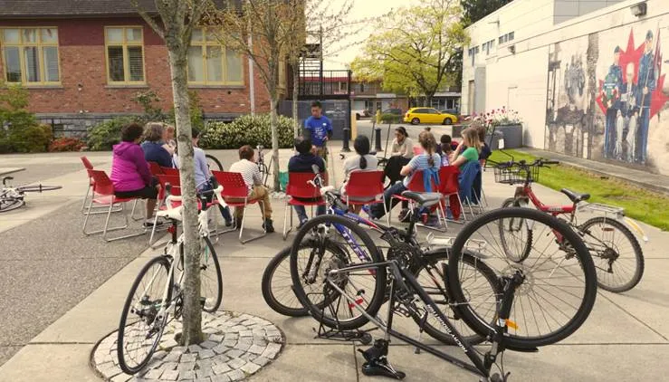 A group of people sit around a circle and listen to an instructor speak.