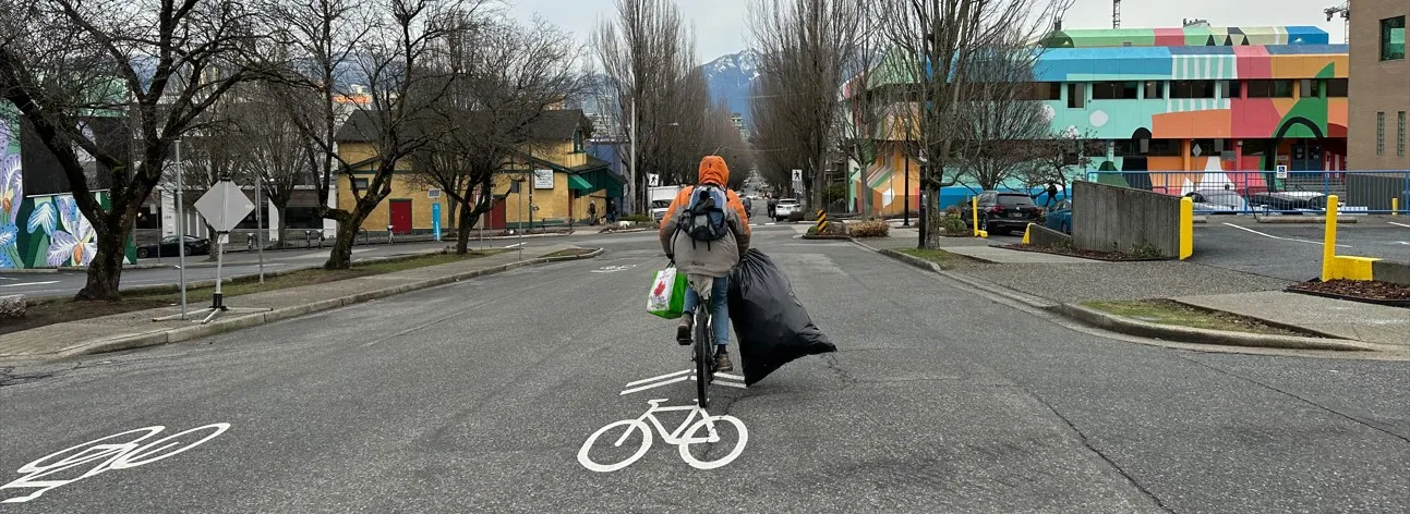 A person rides their bike holding onto a bag of recyclables