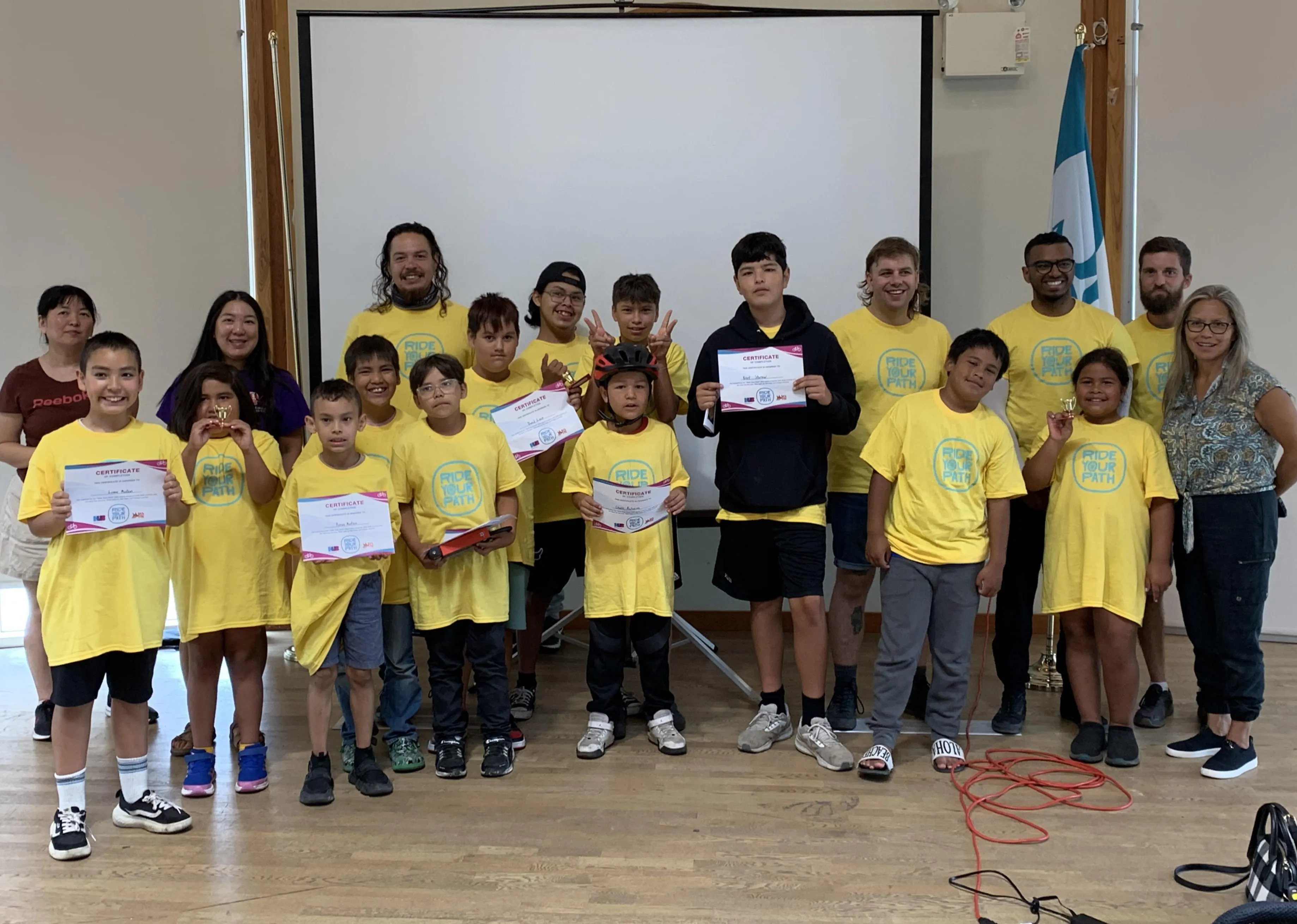 Students, instructors, and teachers pose for a photo in a classroom. Several students are holding up certificates of completion.