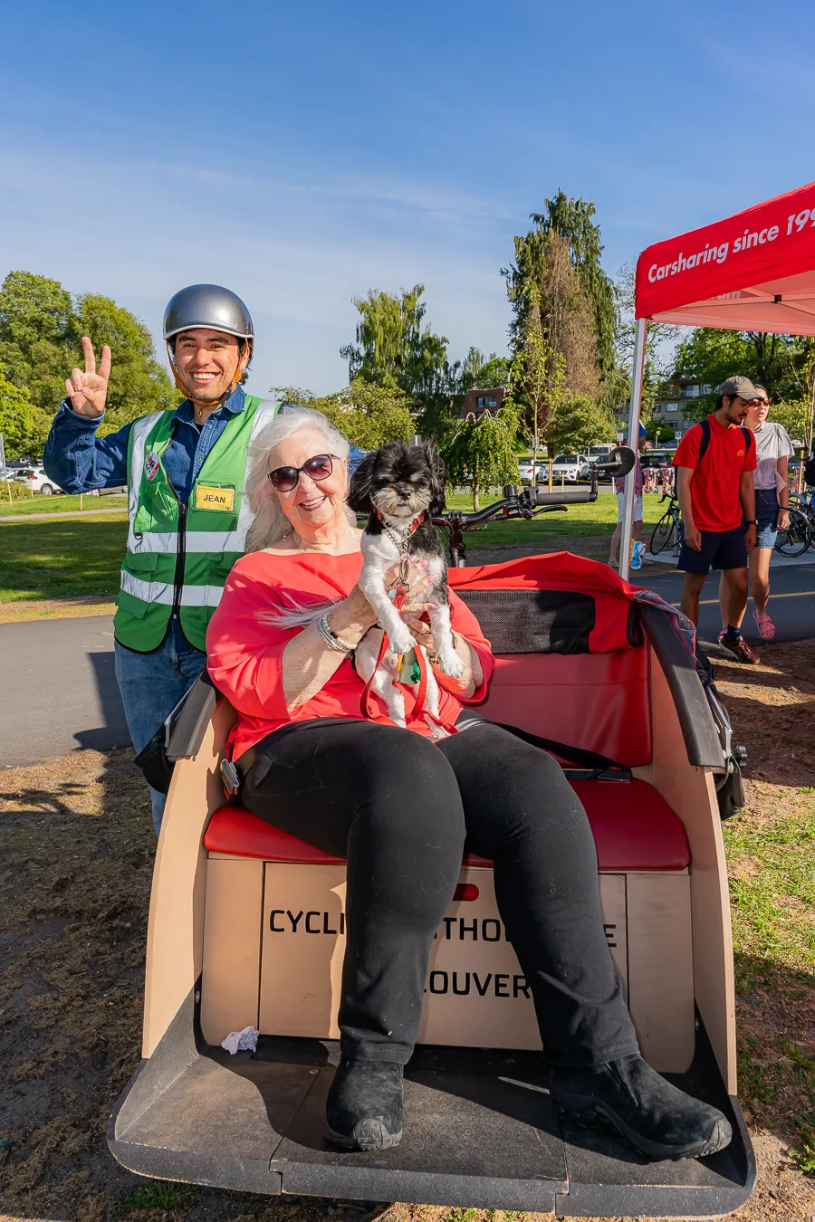A Cycling Without Age volunteer poses with a senior woman and her dog sitting in a tri-shaw bike.