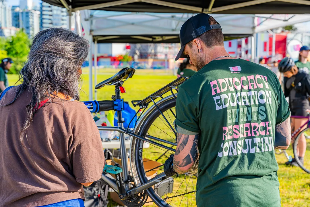 A bike mechanic fixes a woman's bike. The woman stands beside the mechanic.