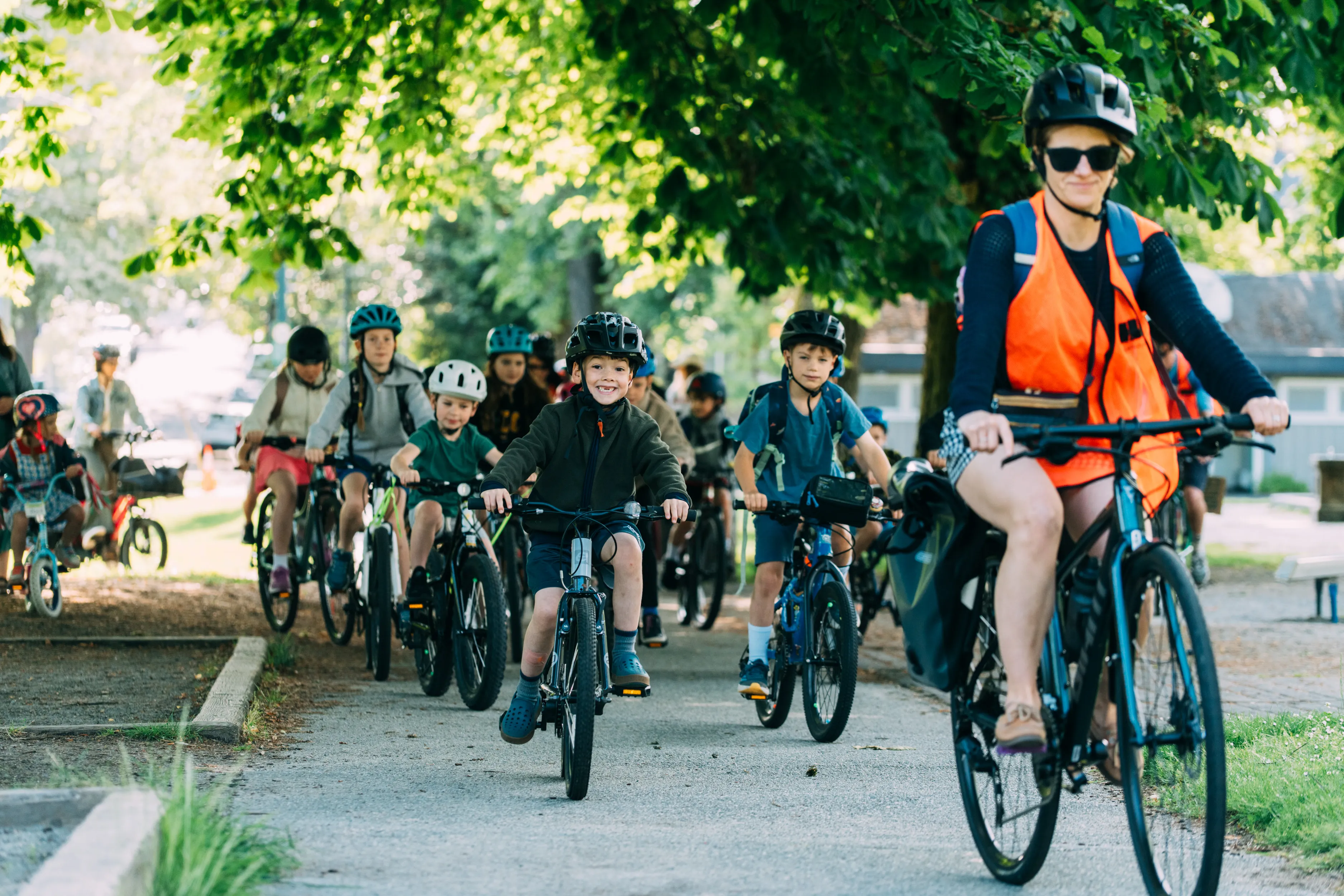 Several students ride their bikes while following an instructor on a multi-use path.