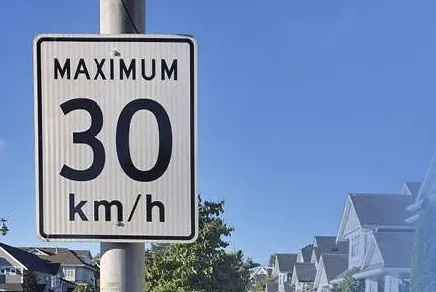 A Maximum 30 km/h sign with residential homes in the background.