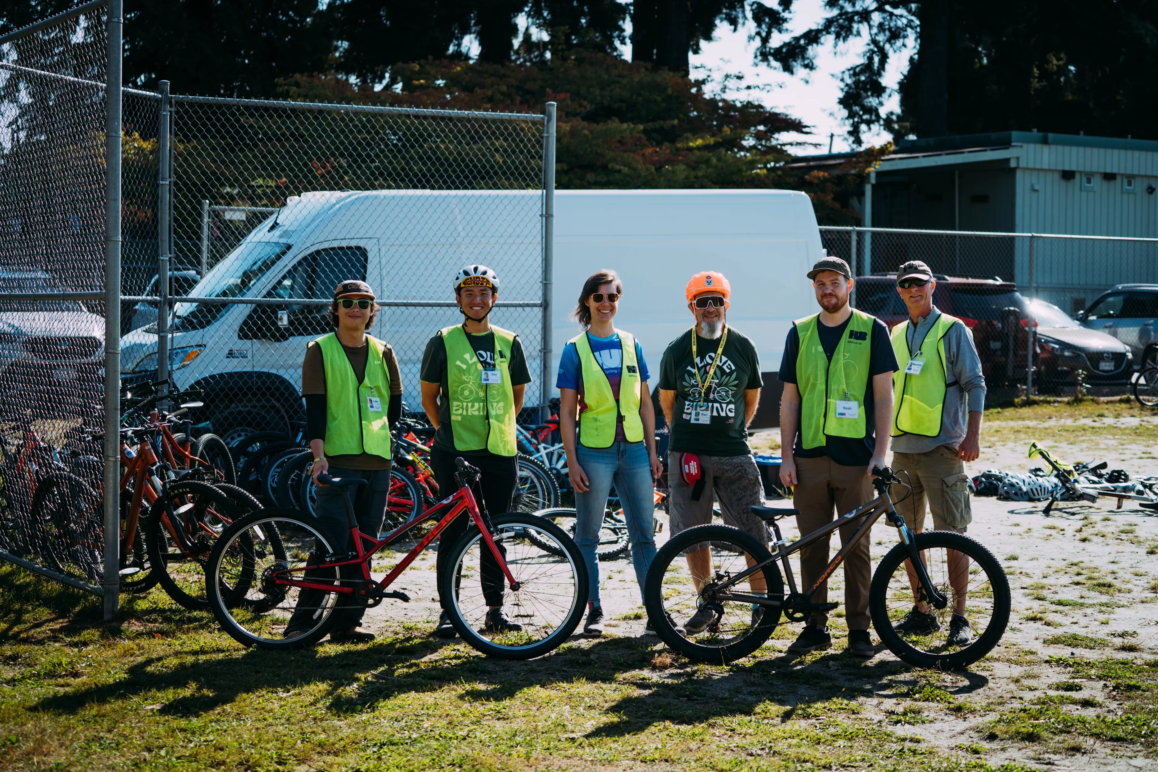 Six instructors stand in a baseball diamond with two bikes. They are all wearing yellow pinnies.